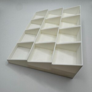 Peut inclure: Pr&eacute;sentoir blanc &agrave; gradins avec plusieurs compartiments rectangulaires. Le pr&eacute;sentoir est inclin&eacute;, chaque niveau de compartiments &eacute;tant l&eacute;g&egrave;rement en retrait. Le design est &eacute;pur&eacute; et minimaliste, adapt&eacute; pour pr&eacute;senter de petits objets.
