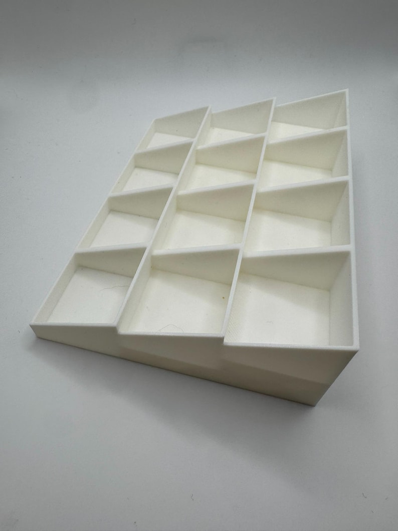 Peut inclure: Pr&eacute;sentoir blanc &agrave; gradins avec plusieurs compartiments rectangulaires. Le pr&eacute;sentoir est inclin&eacute;, chaque niveau de compartiments &eacute;tant l&eacute;g&egrave;rement en retrait. Le design est &eacute;pur&eacute; et minimaliste, adapt&eacute; pour pr&eacute;senter de petits objets.