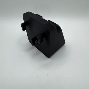 May include: A black, rectangular 3D-printed object with a curved top and two protruding rectangular tabs. The object is set against a white background, showcasing its shape and design. The material appears to be a matte plastic.