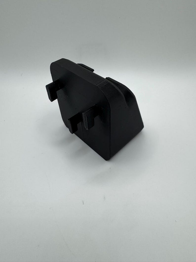 May include: A black, rectangular 3D-printed object with a curved top and two protruding rectangular tabs. The object is set against a white background, showcasing its shape and design. The material appears to be a matte plastic.