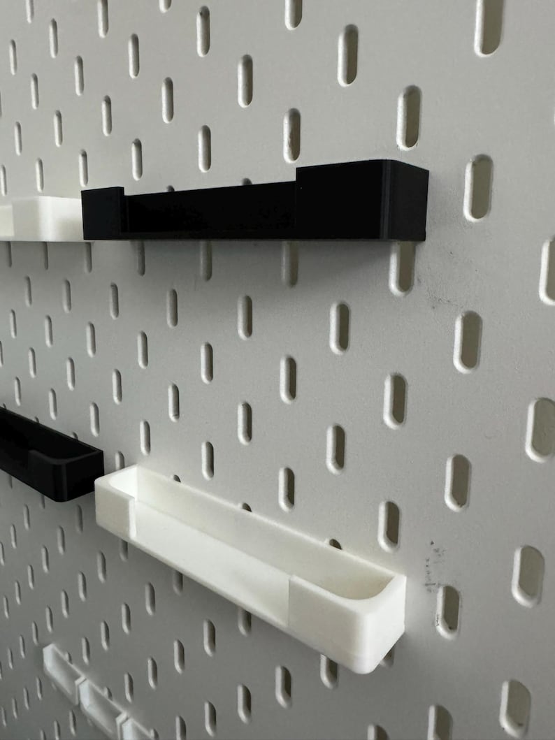 May include: A white pegboard with a series of black and white shelves attached. The shelves are rectangular and designed to fit into the pegboard holes. The shelves are in various sizes and orientations. The pegboard has a series of oval holes.