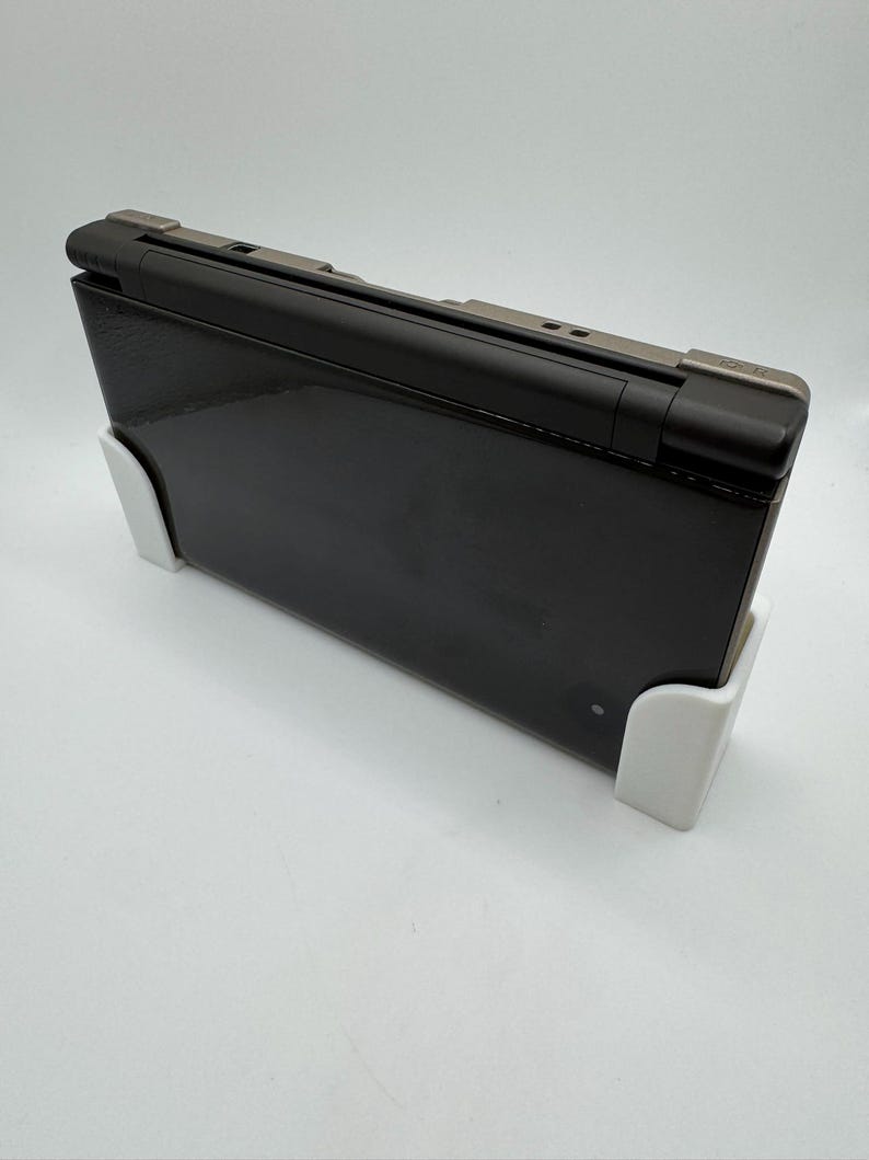 May include: A black laptop computer with a silver hinge is propped up by two white supports. The laptop is closed and has a glossy finish. The supports are rectangular and appear to be made of plastic.