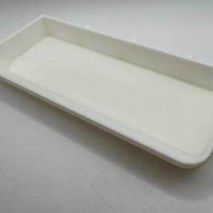 Puede incluir: Una bandeja rectangular blanca con una superficie lisa. La bandeja est&aacute; hecha de un material ligero y tiene un borde ligeramente elevado.