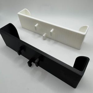 May include: Two rectangular, wall-mounted shelves. One is black, the other white. Each shelf has two hooks and curved end pieces. The shelves are designed to hold items and are made of a solid material.