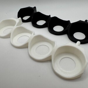 Puede incluir: Dos juegos de tres soportes de pl&aacute;stico blanco y negro impresos en 3D con aberturas circulares. Los soportes est&aacute;n dise&ntilde;ados para sujetar objetos redondos.
