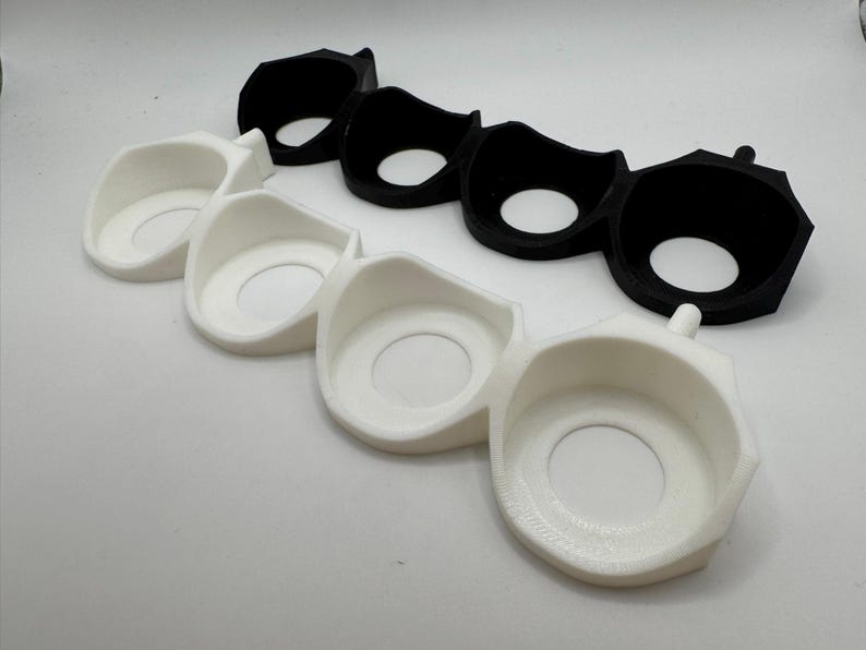 Puede incluir: Dos juegos de tres soportes de pl&aacute;stico blanco y negro impresos en 3D con aberturas circulares. Los soportes est&aacute;n dise&ntilde;ados para sujetar objetos redondos.