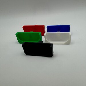 May include: Five plastic storage containers in different colours: red, green, blue, white, and black. The containers are all the same size and shape, and they have a rectangular base and a curved top.