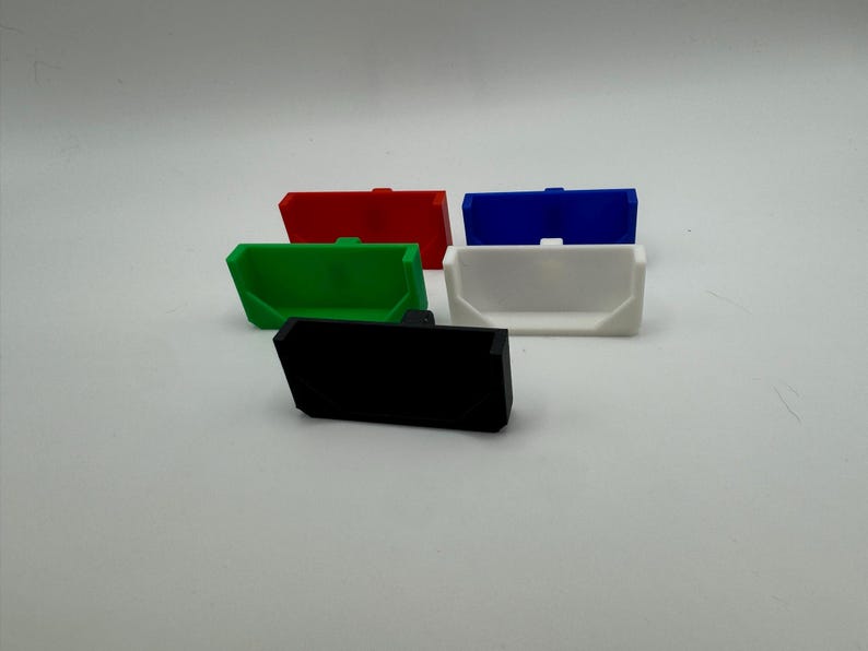 May include: Five plastic storage containers in different colours: red, green, blue, white, and black. The containers are all the same size and shape, and they have a rectangular base and a curved top.
