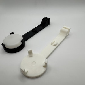 K&ouml;nnte beinhalten: Zwei 3D-gedruckte Handyhalter, einer schwarz und einer wei&szlig;. Beide Halter haben eine runde Basis mit drei Zinken und einen gebogenen Arm.