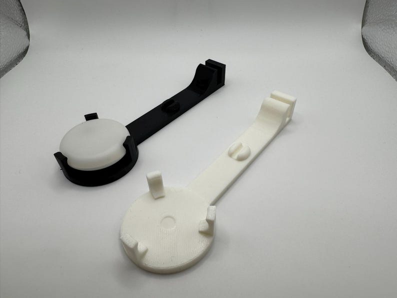 K&ouml;nnte beinhalten: Zwei 3D-gedruckte Handyhalter, einer schwarz und einer wei&szlig;. Beide Halter haben eine runde Basis mit drei Zinken und einen gebogenen Arm.