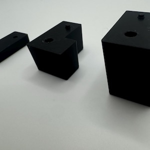 May include: Three black plastic corner brackets of different sizes. The brackets have a right angle shape with a hole in the centre of the top surface.