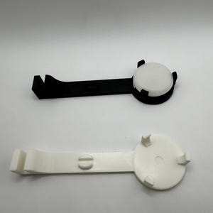 K&ouml;nnte beinhalten: Zwei Plastikclips, einer schwarz und einer wei&szlig;, mit einer runden, flachen, wei&szlig;en Scheibe an jedem Ende. Die Clips sind so konzipiert, dass sie etwas festhalten.