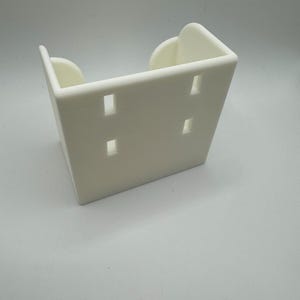May include: A white, rectangular bracket with four evenly spaced rectangular holes. The bracket has rounded edges and a curved design on the top. The object is made of a solid, opaque material.