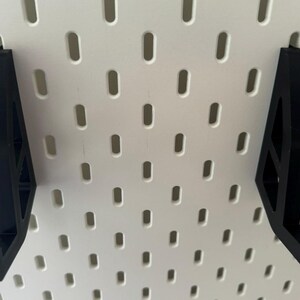 May include: Two black plastic pegboard hooks with a triangular shape and a hook at the bottom.