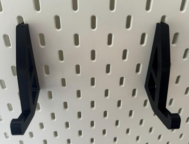 May include: Two black plastic pegboard hooks with a triangular shape and a hook at the bottom.
