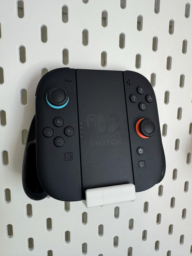 Op de afbeelding: Zwarte Nintendo Switch-controller met blauwe en oranje accenten. De controller heeft knoppen en joysticks en is gemonteerd op een wit pegboard. Het Nintendo Switch-logo is zichtbaar.