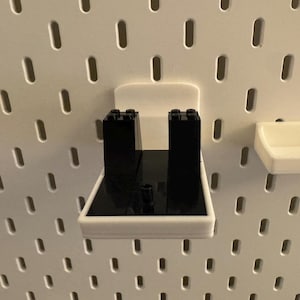 May include: White plastic pegboard accessories, including a shelf and a holder with black blocks. The pegboard has a series of evenly spaced, oblong holes. The shelf and holder are designed to attach to the pegboard.