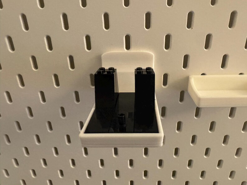May include: White plastic pegboard accessories, including a shelf and a holder with black blocks. The pegboard has a series of evenly spaced, oblong holes. The shelf and holder are designed to attach to the pegboard.