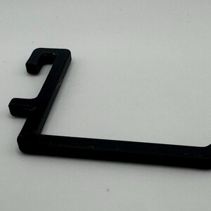 May include: A black plastic hook with a curved shape. The hook is designed to hang items on a wall or shelf.