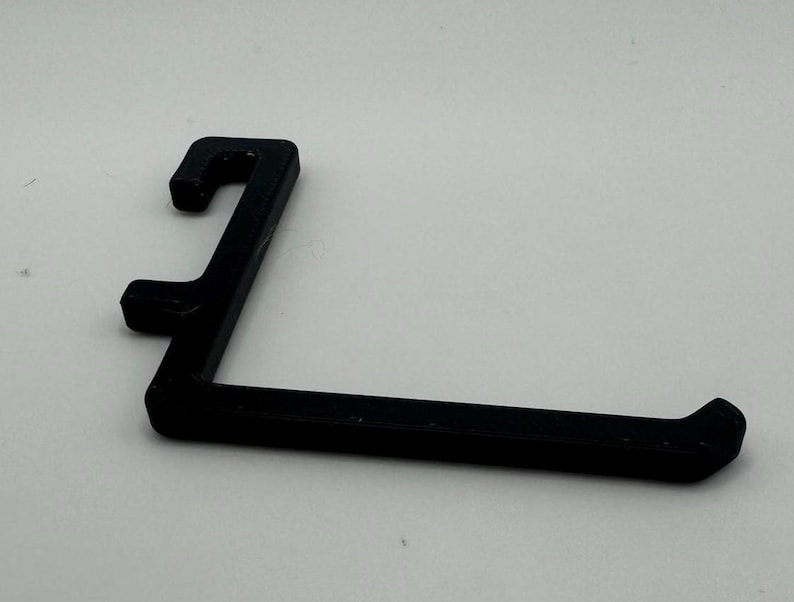 May include: A black plastic hook with a curved shape. The hook is designed to hang items on a wall or shelf.