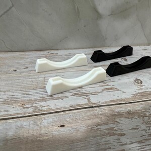 Puede incluir: Cuatro objetos peque&ntilde;os, curvos, en forma de cuna. Dos son blancos y dos son negros. Est&aacute;n dispuestos sobre una superficie de madera clara y envejecida. Los objetos tienen un dise&ntilde;o minimalista, con un acabado liso y mate.