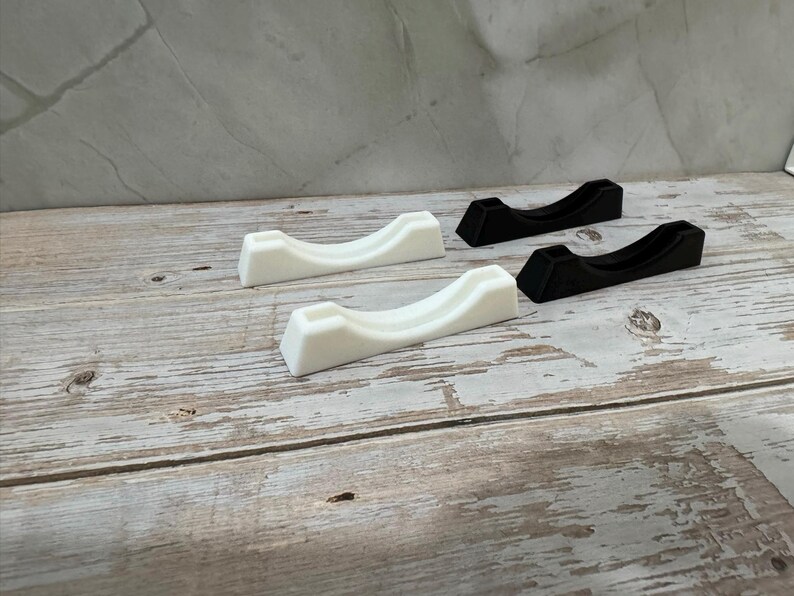 Puede incluir: Cuatro objetos peque&ntilde;os, curvos, en forma de cuna. Dos son blancos y dos son negros. Est&aacute;n dispuestos sobre una superficie de madera clara y envejecida. Los objetos tienen un dise&ntilde;o minimalista, con un acabado liso y mate.