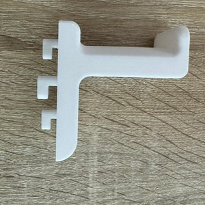 Pu&ograve; includere: Una staffa angolare bianca in plastica. Presenta tre piccole sporgenze rettangolari su un lato e un'estremit&agrave; curva sull'altro. Progettata per il montaggio su superficie, &egrave; probabilmente un componente di mobili.