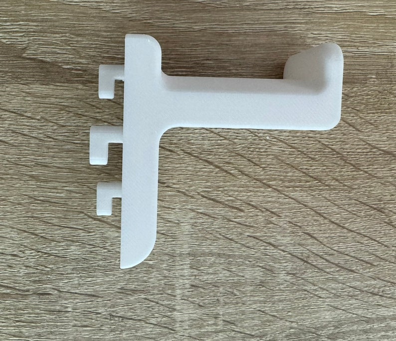 Pu&ograve; includere: Una staffa angolare bianca in plastica. Presenta tre piccole sporgenze rettangolari su un lato e un'estremit&agrave; curva sull'altro. Progettata per il montaggio su superficie, &egrave; probabilmente un componente di mobili.