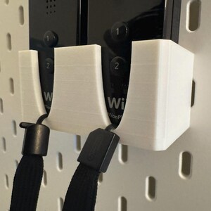 Puede incluir: Soporte de pared blanco impreso en 3D para dos mandos de Wii. El soporte tiene dos cunas dise&ntilde;adas para sujetar los mandos de forma segura. Se adjuntan cordones negros. El fondo es una placa perforada blanca.