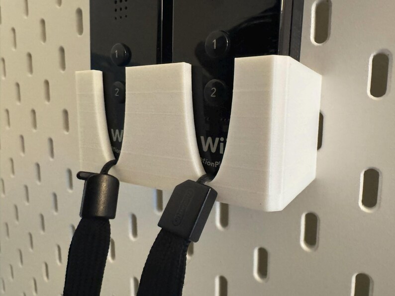 Puede incluir: Soporte de pared blanco impreso en 3D para dos mandos de Wii. El soporte tiene dos cunas dise&ntilde;adas para sujetar los mandos de forma segura. Se adjuntan cordones negros. El fondo es una placa perforada blanca.