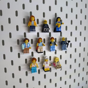 K&ouml;nnte beinhalten: Eine Sammlung farbenfroher Lego-Minifiguren, jede mit einzigartigen Outfits und Accessoires, ist auf einer wei&szlig;en Lochwand angeordnet. Die Figuren umfassen verschiedene Berufe und Stile und zeigen eine vielf&auml;ltige Auswahl an Charakteren.
