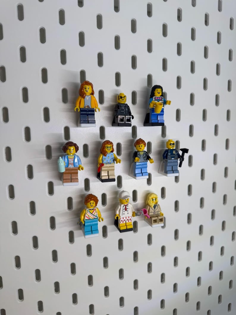 K&ouml;nnte beinhalten: Eine Sammlung farbenfroher Lego-Minifiguren, jede mit einzigartigen Outfits und Accessoires, ist auf einer wei&szlig;en Lochwand angeordnet. Die Figuren umfassen verschiedene Berufe und Stile und zeigen eine vielf&auml;ltige Auswahl an Charakteren.