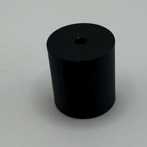 May include: A black cylindrical bottle stopper with a small hole in the center.