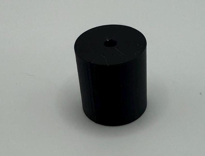 May include: A black cylindrical bottle stopper with a small hole in the center.