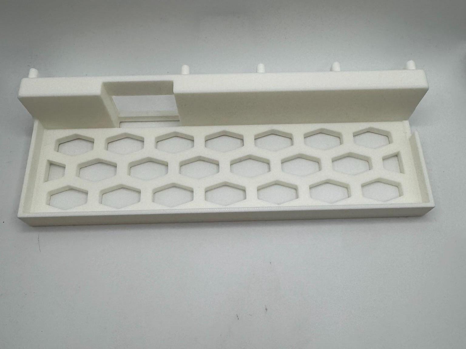 Puede incluir: Bandeja blanca rectangular con patr&oacute;n de panal y secci&oacute;n elevada con abertura rectangular. La bandeja tiene peque&ntilde;os pasadores a lo largo del borde superior. Probablemente de pl&aacute;stico.