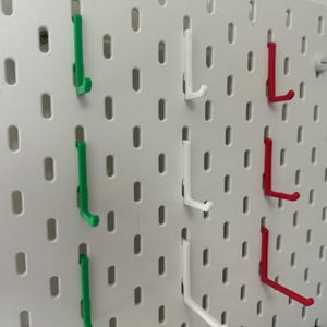 May include: A white pegboard with three rows of hooks. The hooks are in three colors: green, white, and red.