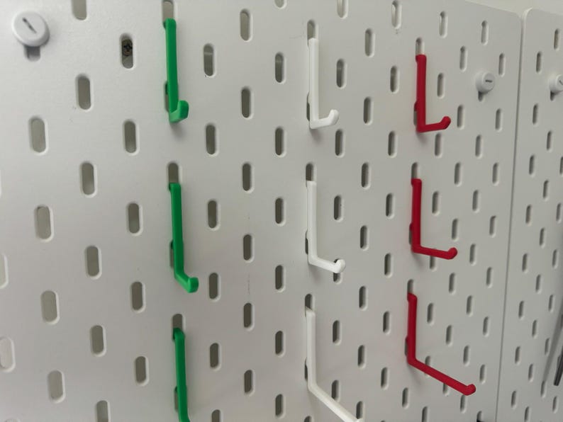 May include: A white pegboard with three rows of hooks. The hooks are in three colors: green, white, and red.