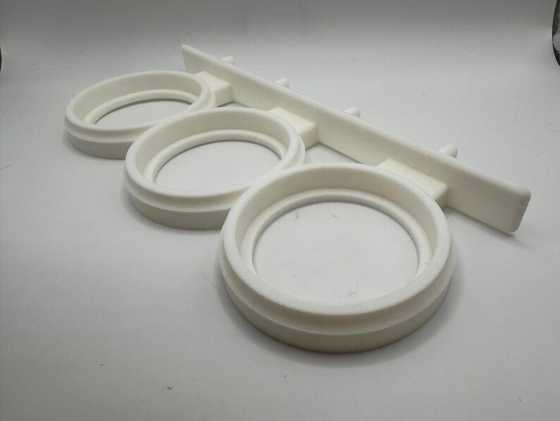 May include: White plastic wall-mounted organizer with three circular slots for holding items.