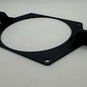 以下が含まれることがあります： 黒色のプラスチック製のファンマウントで、両側に2つの突出したタブがあります。マウントの中央には円形の開口部があります。