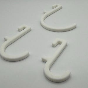 Puede incluir: Tres ganchos de pl&aacute;stico blanco con un dise&ntilde;o en forma de J. Los ganchos est&aacute;n dise&ntilde;ados para colgar art&iacute;culos en una pared u otra superficie.