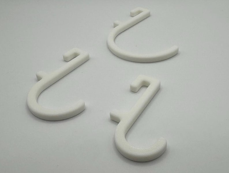 Puede incluir: Tres ganchos de pl&aacute;stico blanco con un dise&ntilde;o en forma de J. Los ganchos est&aacute;n dise&ntilde;ados para colgar art&iacute;culos en una pared u otra superficie.