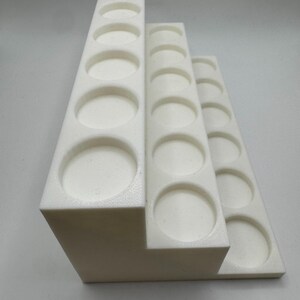 Puede incluir: Un organizador blanco en niveles con m&uacute;ltiples aberturas circulares. El organizador est&aacute; dise&ntilde;ado para guardar objetos peque&ntilde;os, con cada nivel con un n&uacute;mero diferente de aberturas. La estructura est&aacute; hecha de un material s&oacute;lido y opaco.
