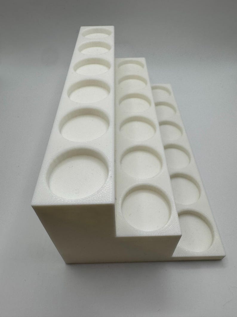 Puede incluir: Un organizador blanco en niveles con m&uacute;ltiples aberturas circulares. El organizador est&aacute; dise&ntilde;ado para guardar objetos peque&ntilde;os, con cada nivel con un n&uacute;mero diferente de aberturas. La estructura est&aacute; hecha de un material s&oacute;lido y opaco.