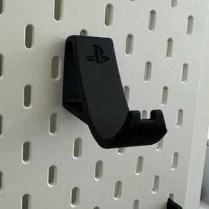 May include: Black plastic wall mount for a PlayStation controller. The mount has a PlayStation logo on the front.