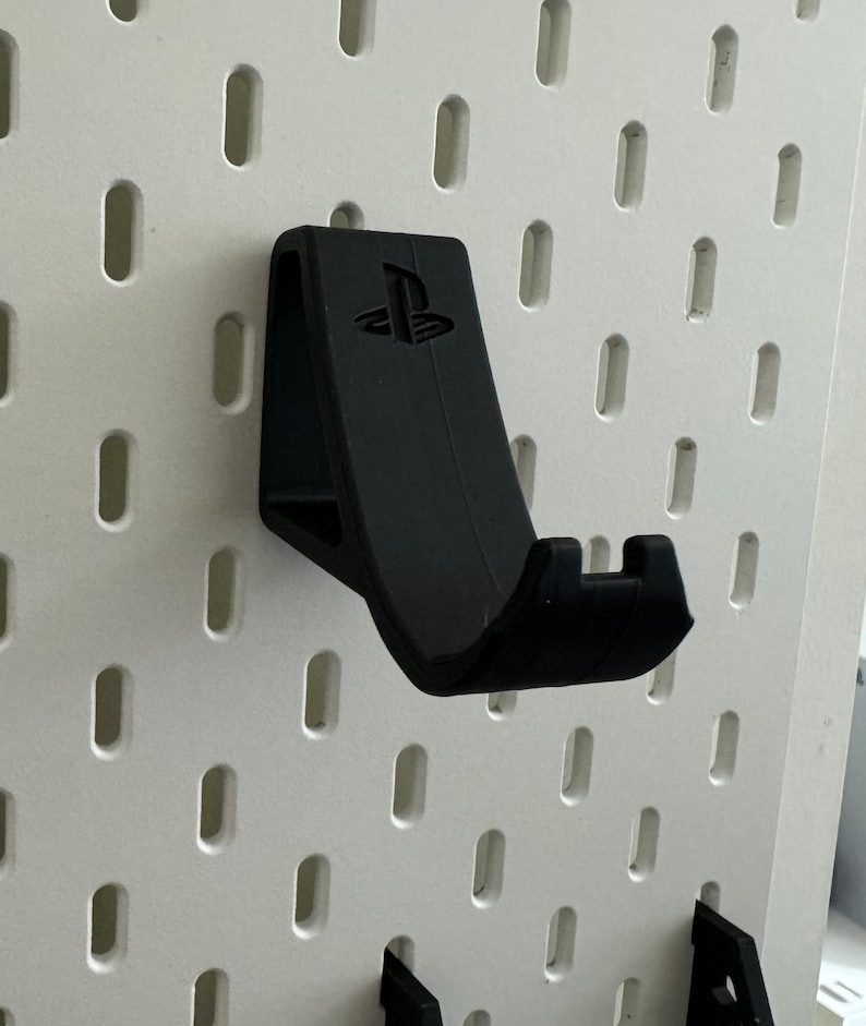 May include: Black plastic wall mount for a PlayStation controller. The mount has a PlayStation logo on the front.