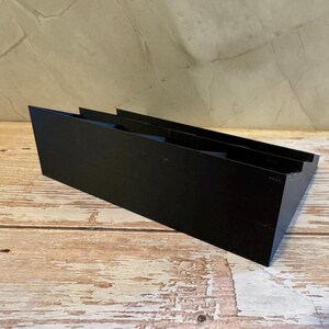 Peut inclure: Un objet rectangulaire noir et inclin&eacute; avec deux rainures parall&egrave;les. L'objet est fait d'un mat&eacute;riau solide et repose sur une surface en bois. L'arri&egrave;re-plan est un mur de couleur claire.