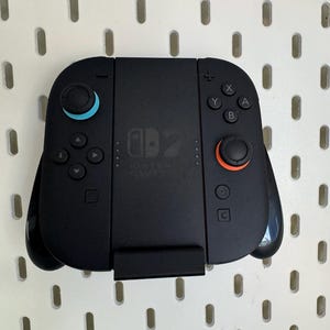 Op de afbeelding: Zwarte Nintendo Switch-controller met blauwe en oranje accenten. Voorzien van knoppen, directionele pads en analoge sticks. De controller heeft het Nintendo Switch-logo en is voor gaming.
