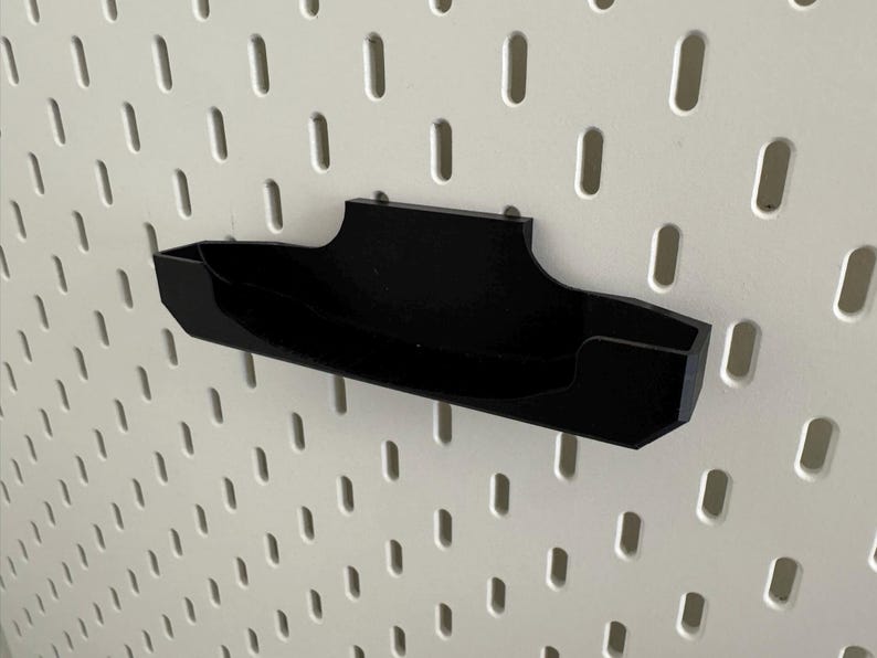Op de afbeelding: Een zwarte, wandgemonteerde organizer van plastic met een gebogen ontwerp. De organizer is gemonteerd op een wit prikbord.