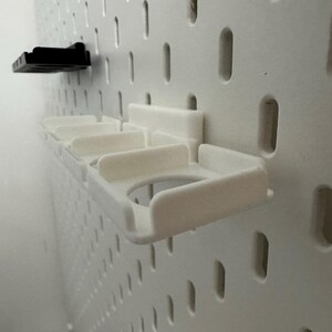 K&ouml;nnte beinhalten: Wei&szlig;e Lochwand mit zwei angebrachten Kunststoff-Organizern. Einer ist schwarz und der andere wei&szlig; mit mehreren F&auml;chern. Die Lochwand hat gleichm&auml;&szlig;ig verteilte L&ouml;cher zur Befestigung von Zubeh&ouml;r.