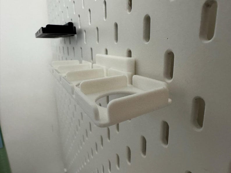 K&ouml;nnte beinhalten: Wei&szlig;e Lochwand mit zwei angebrachten Kunststoff-Organizern. Einer ist schwarz und der andere wei&szlig; mit mehreren F&auml;chern. Die Lochwand hat gleichm&auml;&szlig;ig verteilte L&ouml;cher zur Befestigung von Zubeh&ouml;r.